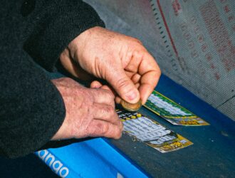 Hands using a coin to scratch off a lottery ticket on a blue table.